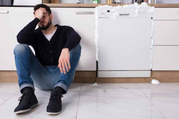 Dishwasher overflowing with water spilling onto the kitchen floor.